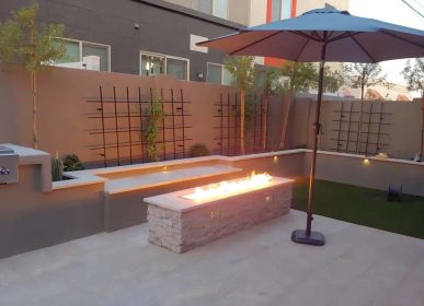 A backyard featuring a cozy fire pit surrounded by seating and a large umbrella for shade.