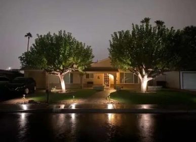 A house illuminated at night, with lights shining along the driveway, creating a warm and inviting atmosphere.