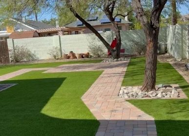 Artificial grass in a backyard, featuring a neatly laid brick walkway for easy access and aesthetic appeal.