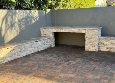 A brick patio featuring a stone fireplace and a wooden bench for seating.